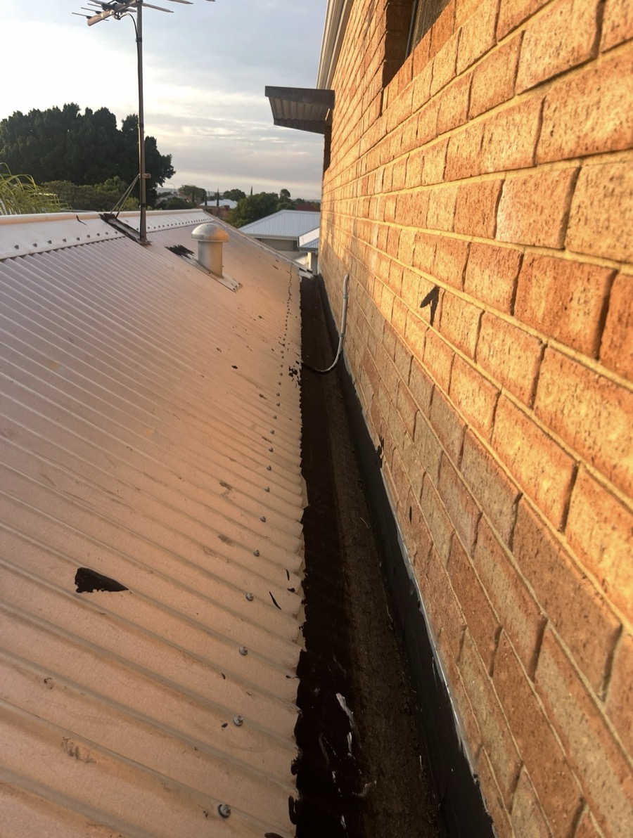 Before: Box gutter against a brick wall, patched with black tar
