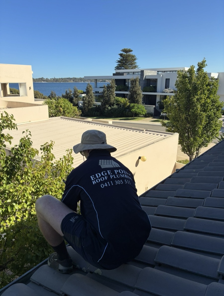 An Edge Point roof plumber in a branded shirt working on a tiled roof, with river views behind