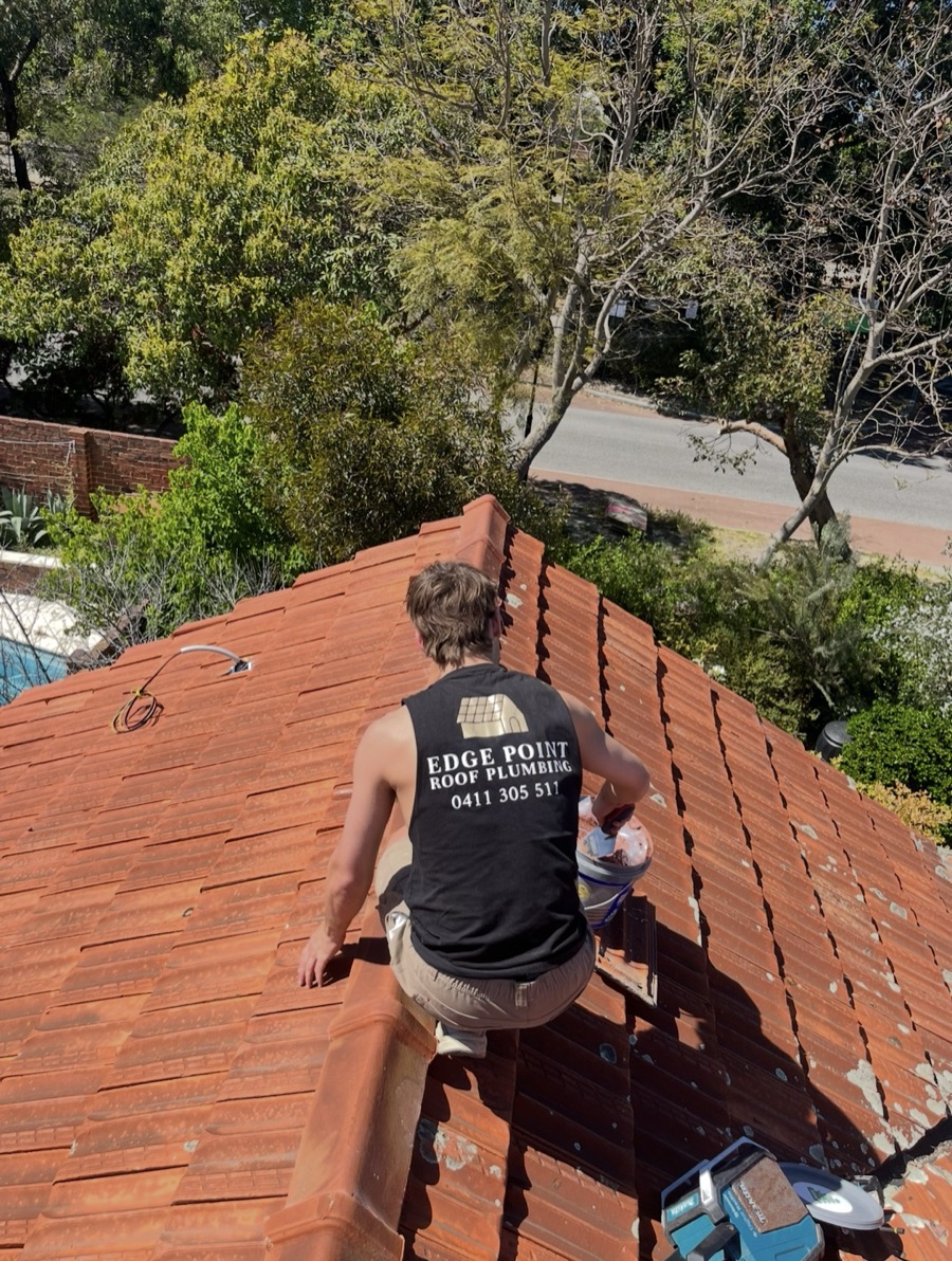An Edge Point roof plumber repointing ridge caps on a terracotta tiled roof